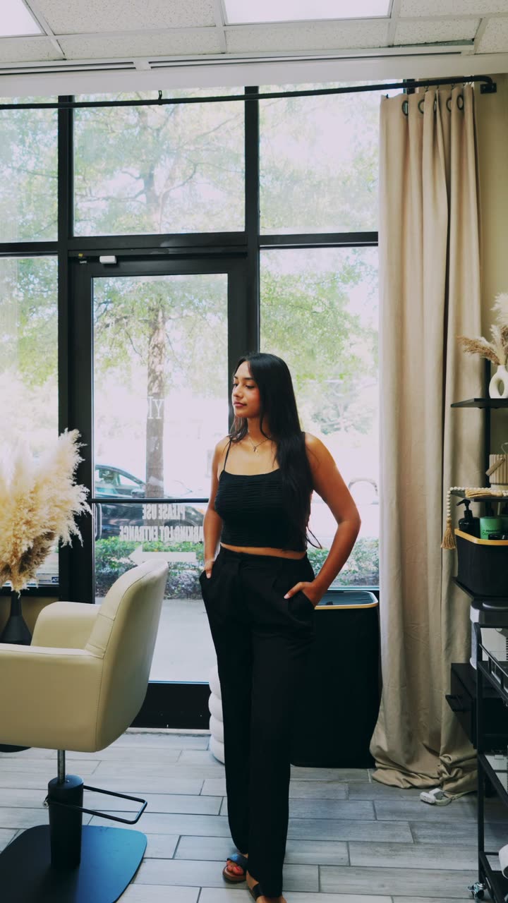 Stylist standing in a styled suite with a window wall, styling chair and tall curtains